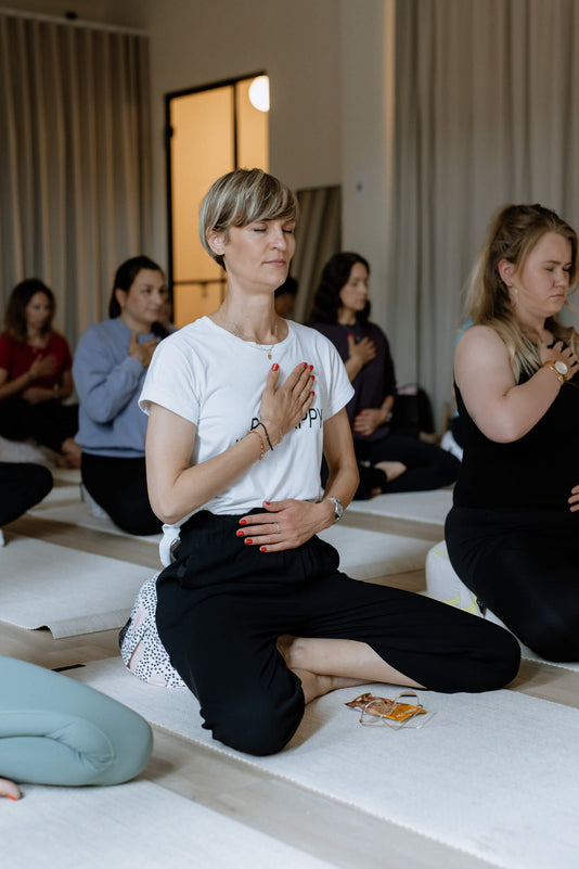 Mehrere Frauen sitzen auf Yoga Blöcken und Matten und meditieren