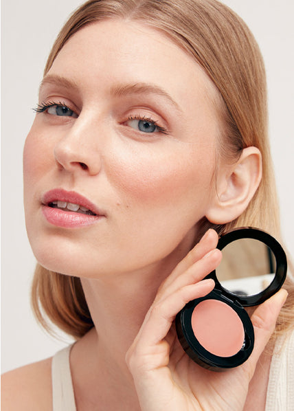 Frau hält JACKS beauty line Cream Blush in Peach in ihrer Hand vor ihrem Gesicht