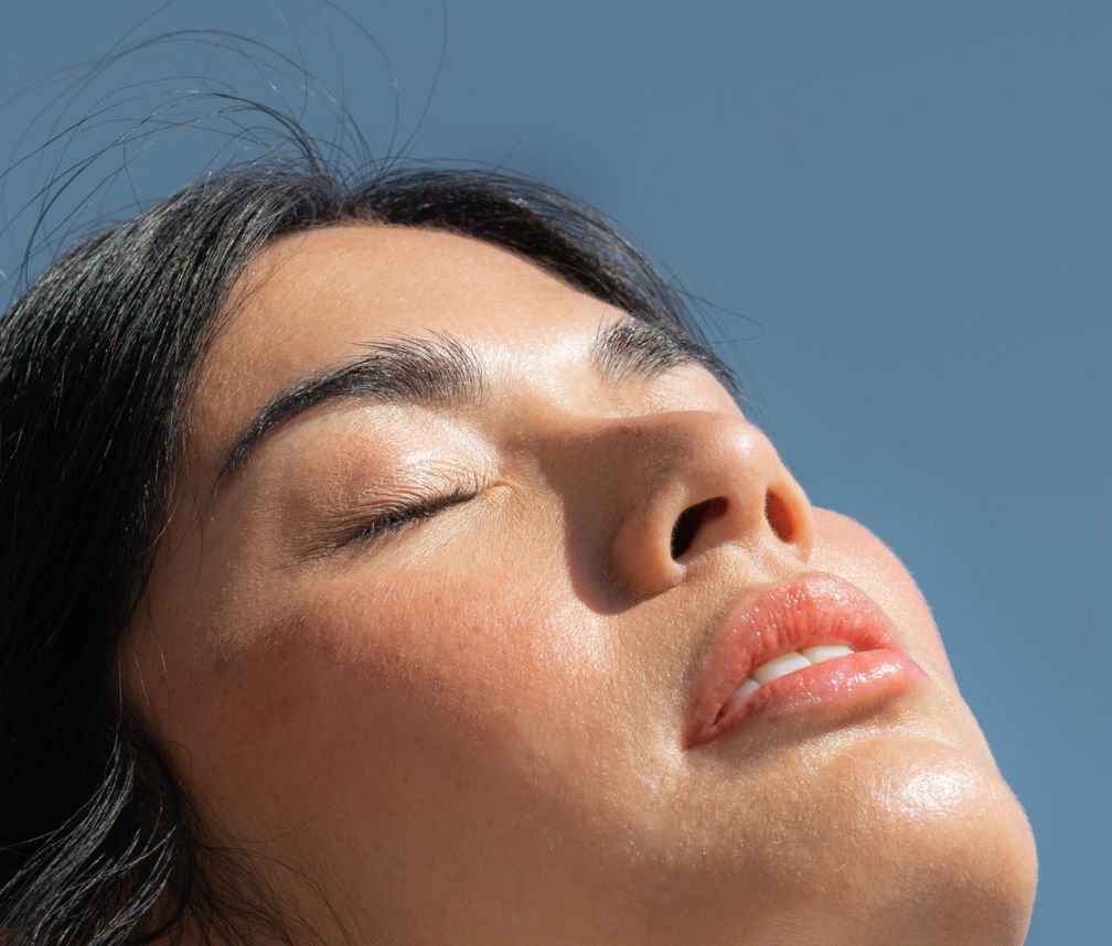 Sonne strahlt ins Gesicht einer schwarzhaarigen Frau mit geschlossenen Augen Sonne strahlt ins Gesicht einer schwarzhaarigen Frau mit geschlossenen Augen