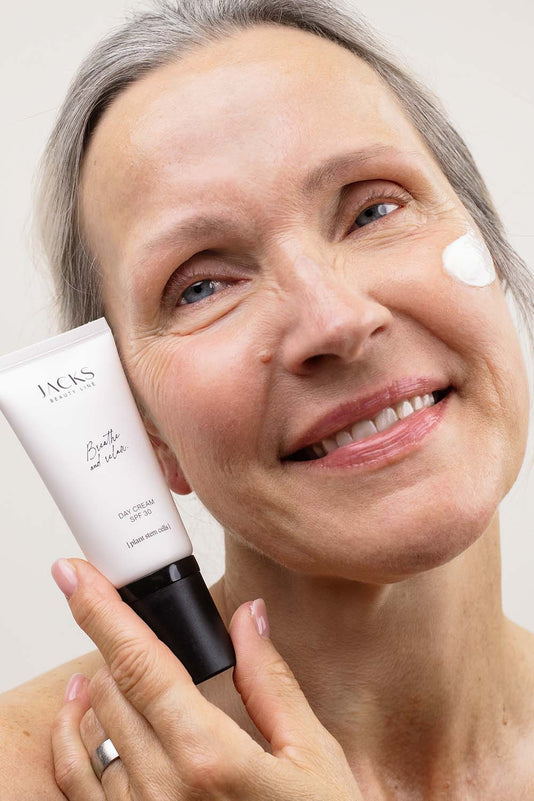 Ältere Frau trägt die JACKS beauty line Tagescreme mit LSF 30 im und Flakon neben ihr Gesicht