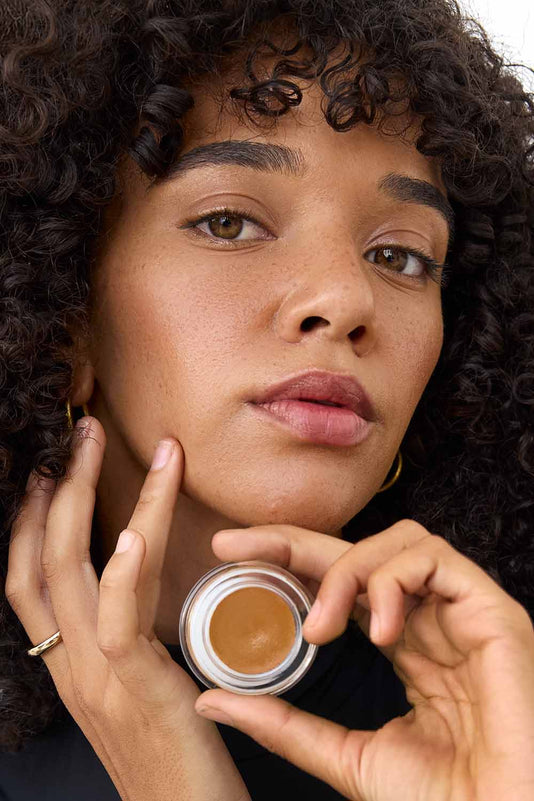 #farbwunsch_n-6, Frau trägt Cover Concealer N6 und hält Concealer Tiegel vor ihr Gesicht