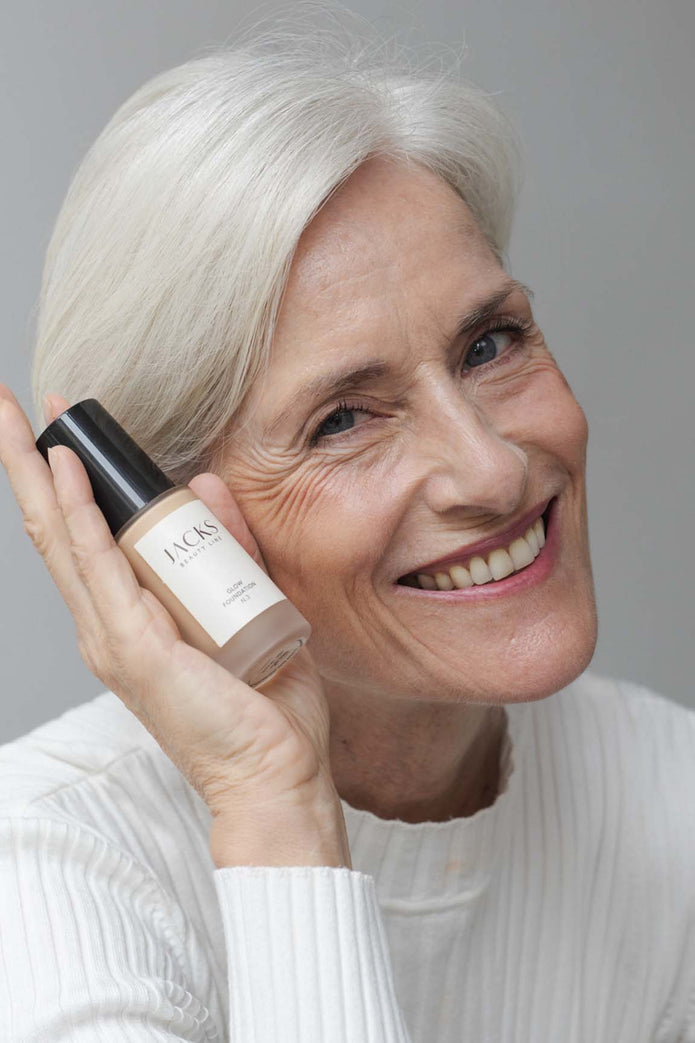 Ältere Frau trägt JACKS beauty line Glow Foundation im Gesicht und Flakon in der Hand