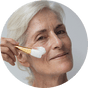Ü50 Frau trägt die JACKS beauty line Glow Mask mit einem Maskenpinsel auf Ü50 Frau trägt die JACKS beauty line Glow Mask mit einem Maskenpinsel auf