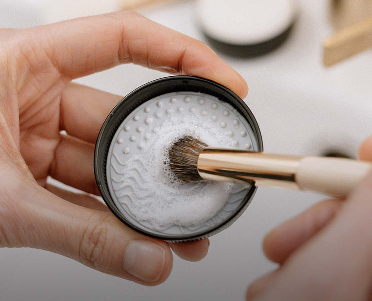 Frau reinigt Make-up Pinsel mit einem Silikonpad und Seife