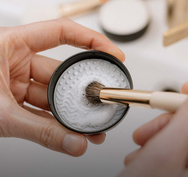 Frau reinigt Make-up Pinsel mit einem Silikonpad und Seife