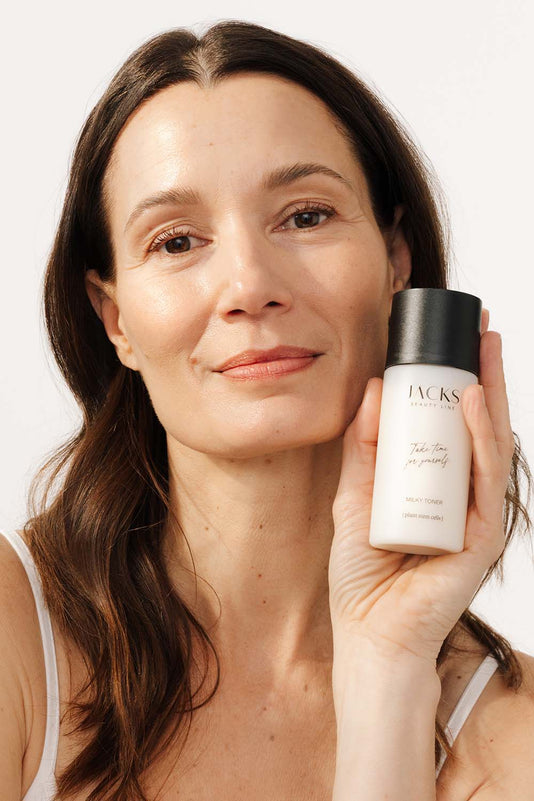 Frau hält JACKS beauty line Milky Toner in der Hand neben ihr Gesicht