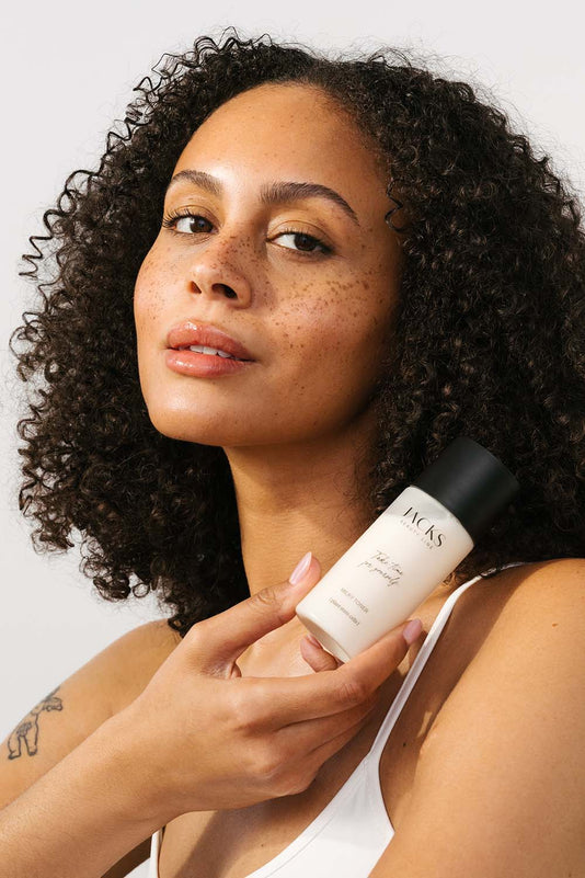 Frau mit dunkelbraunen Locken hält den JACKS beauty line Milky Toner in den Händen