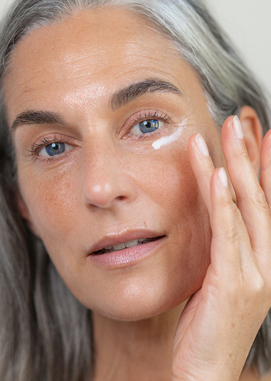 Frau Ü40 trägt sich Augencreme mit ihren Händen unter ihre Augen auf