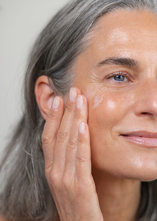 Frau Ü40 trägt sich Creme mit ihren Händen auf ihre Gesichtshaut auf