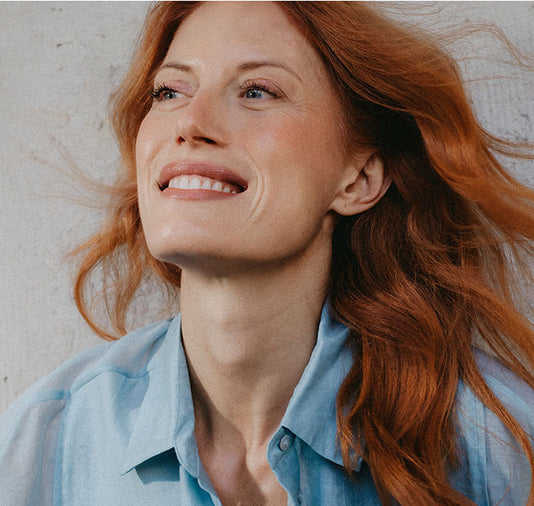 Rothaaige Frau mit hellblauer Bluse und geschminktem Gesicht