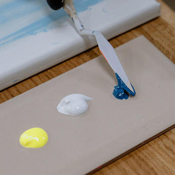 Neongelbe, weiße und blaue Farbe auf einer Mischplatte mit Spatel Neongelbe, weiße und blaue Farbe auf einer Mischplatte mit Spatel