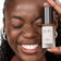 #farbwunsch_n-9, #farbwunsch_dunkler-hauttyp, #farbwunsch_sehr-dunkler-hauttyp, Frau trägt JACKS beauty line Glow Foundation im Gesicht und Flakon in der Hand
