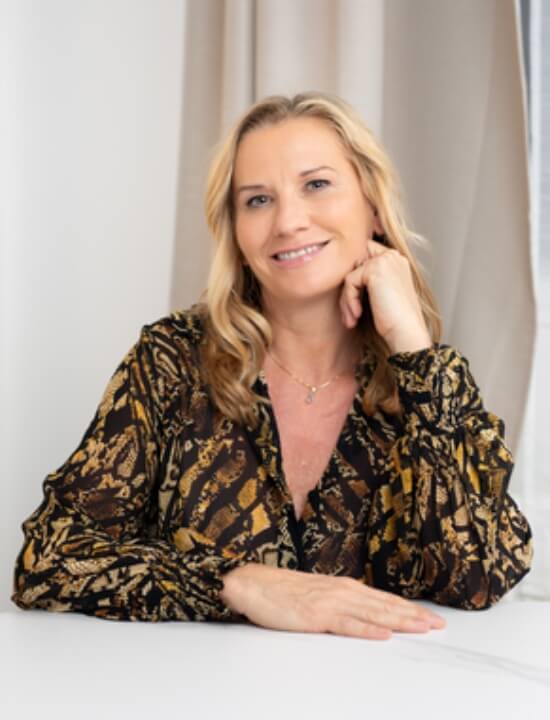 Coach Peggy Reichelt trägt eine gemusterte Bluse und lächelt in die Kamera