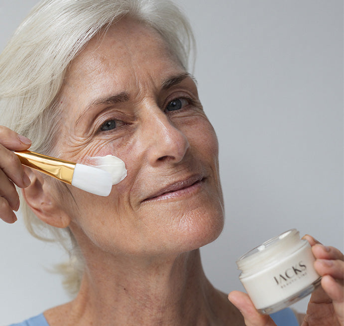 Frau trägt JACKS beauty line Glow Mask mit einem Maskenpinsel auf das Gesicht auf