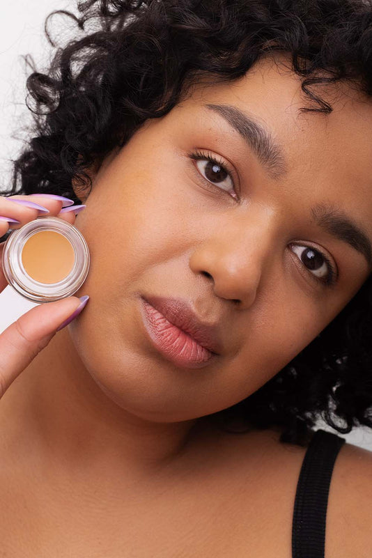 #farbwunsch_n-6, Frau trägt Cover Concealer Farbe N.6 und hält Concealer Tiegel in der Hand