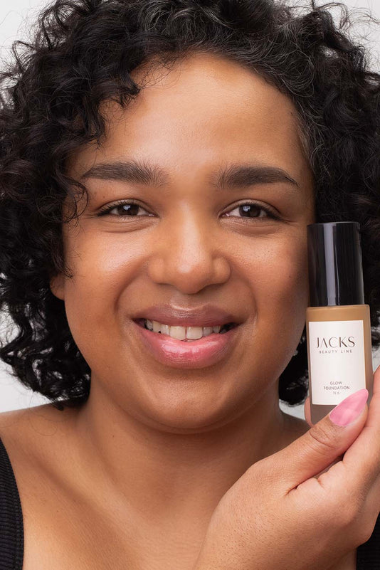 #farbwunsch_n-6, #farbwunsch_dunkler-hauttyp, Frau trägt JACKS beauty line Glow Foundation im Gesicht und Flakon in der Hand