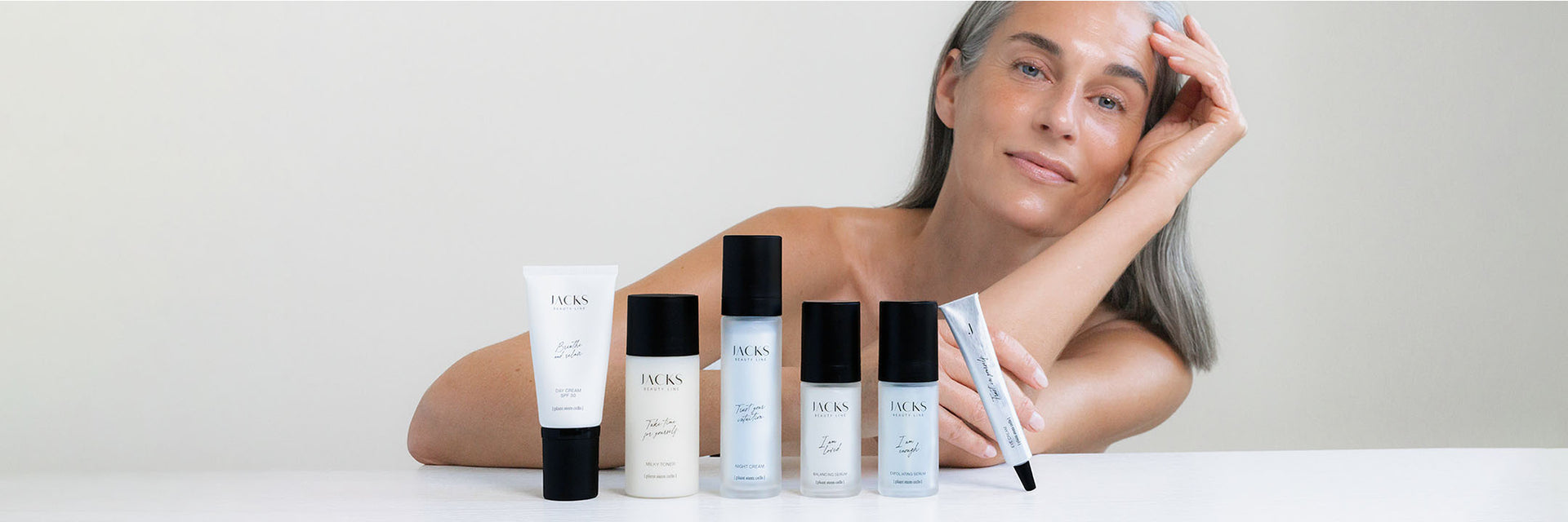 Frau mit strahlender Haut lehnt auf einem Tisch hinter der JACKS beauty line Skincare