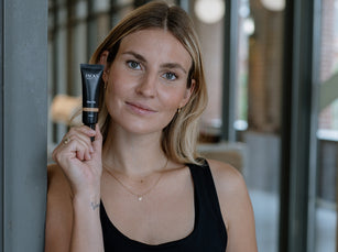 Blonde Frau hält das JACKS beauty line Skin Tint in der Hand neben ihr Gesicht