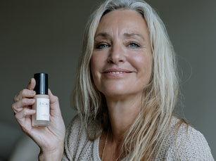 Blonde Frau hält die JACKS beauty line Glow Foundation in der Hand neben ihr Gesicht
