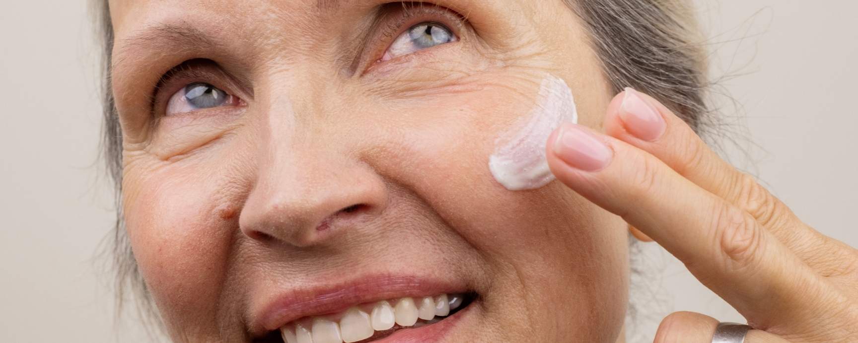 Eine Ältere Frau trägt sich Gesichtscreme auf ihre Wange auf