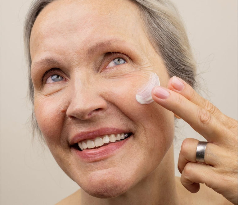 Eine Ältere Frau trägt sich Gesichtscreme auf ihre Wange auf