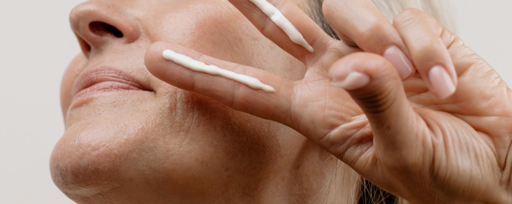 Frau zeigt ein Peace Zeichen und hat zwei Fingerlängen Creme auf Zeige- und Mittelfinger