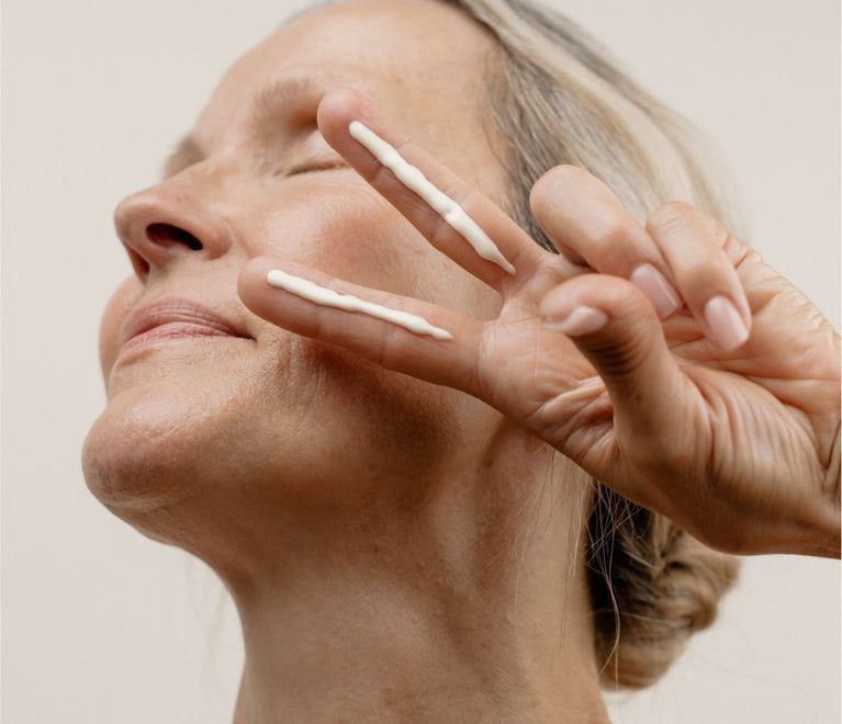 Frau zeigt ein Peace Zeichen und hat zwei Fingerlängen Creme auf Zeige- und Mittelfinger