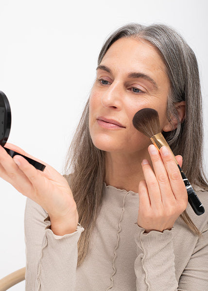 Eine Frau hält den JACKS beauty line Bronzerpinsel in der Hand und trägt Bronzer auf