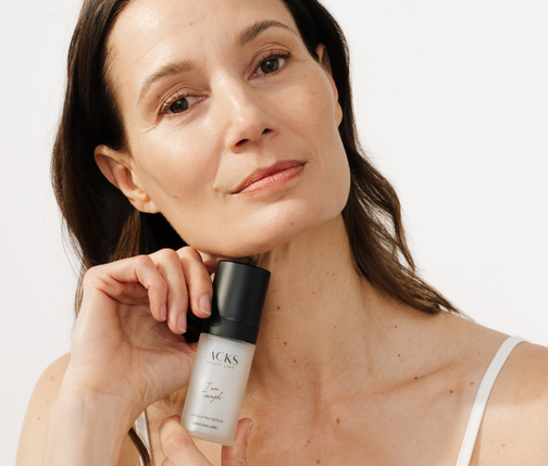 braunhaarige Frau hält JACKS beauty line Exfoliating Serum unter ihrem Gesicht