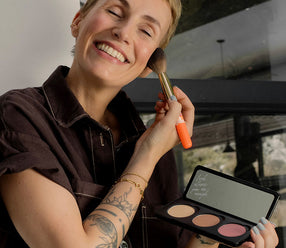Miriam Jacks hält die Individual Powder Palette und trägt sich Blush mit dem Puderpinsel auf