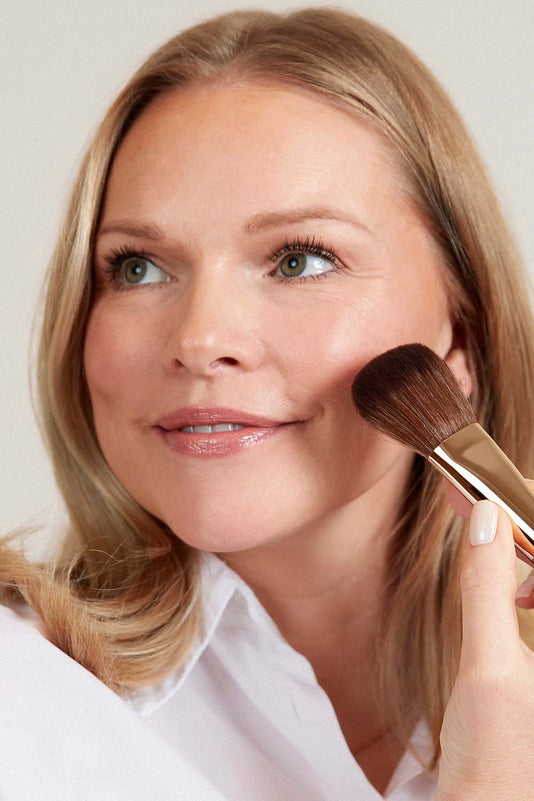 Frau trägt JACKS beauty line Bronzer mit dem #14 Puder- und Bronzerpinsel auf