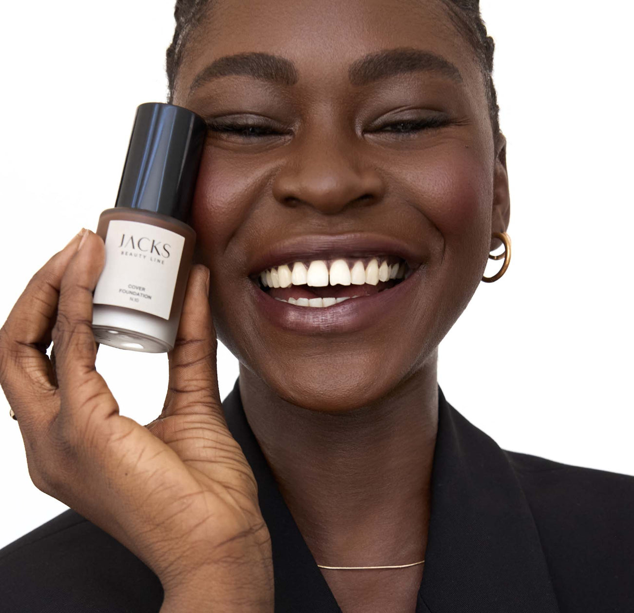 Schwarze Frau lächelt und hält die JACKS beauty line Cover Foundation neben ihr Gesicht