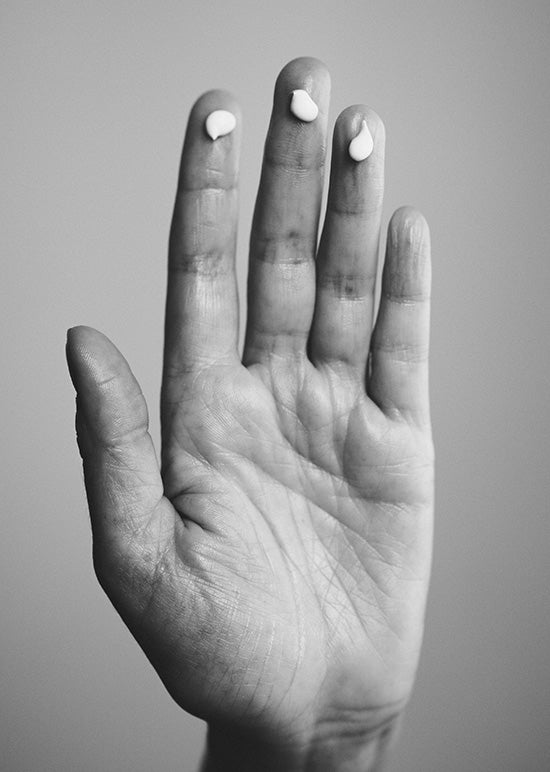 Close-up einer Hand mit Falten und drei Cremepunkten auf drei Fingerkuppen