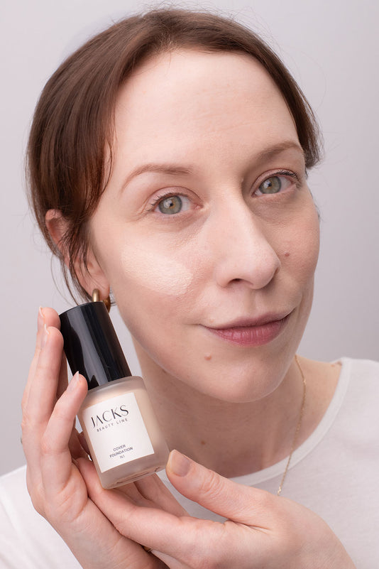 #farbwunsch_n-1, Frau mit JACKS beauty line Cover Foundation N.1 Swatch im Gesicht und Flakon in der Hand