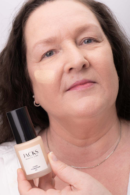 #farbwunsch_n-2, Frau mit JACKS beauty line Cover Foundation N.2 Swatch im Gesicht und Flakon in der Hand