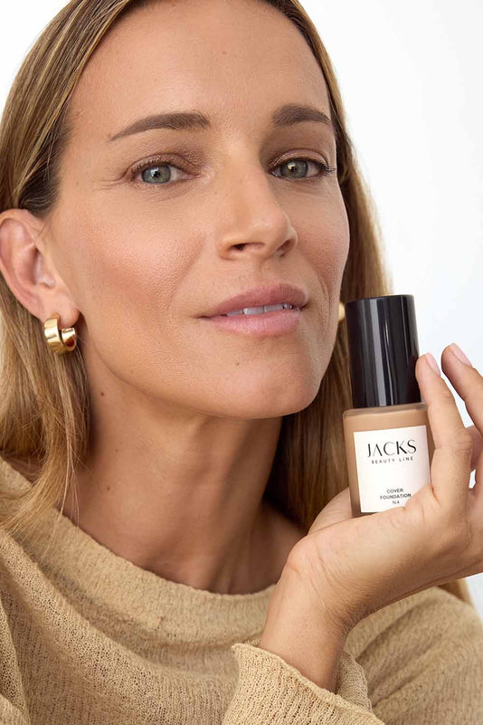 #farbwunsch_n-4, Frau hält JACKS beauty line Cover Foundation N2 Flakon neben ihrem Gesicht