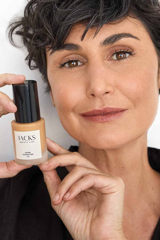 #farbwunsch_n-5, Frau hält JACKS beauty line Cover Foundation N2 Flakon neben ihrem Gesicht