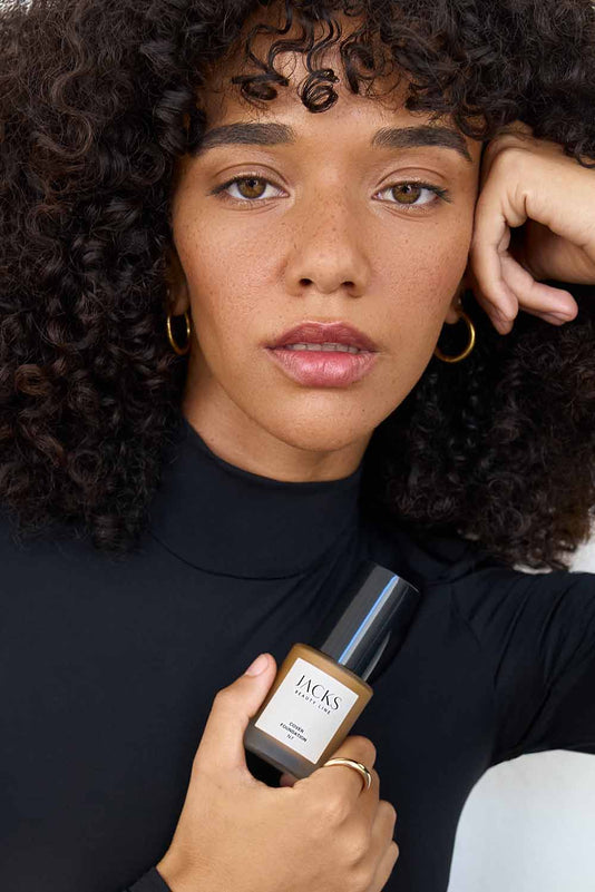 #farbwunsch_n-6, Frau hält JACKS beauty line Cover Foundation N6 Flakon vor ihrem Oberkörper