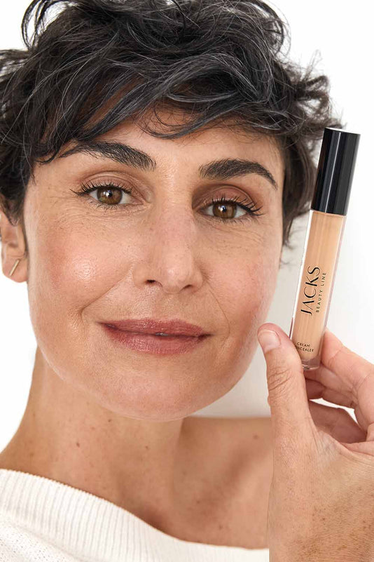 #farbwunsch_n-5, Frau dunklen Haaren hält den JACKS beauty line Cream Concealer N5 neben ihr Gesicht