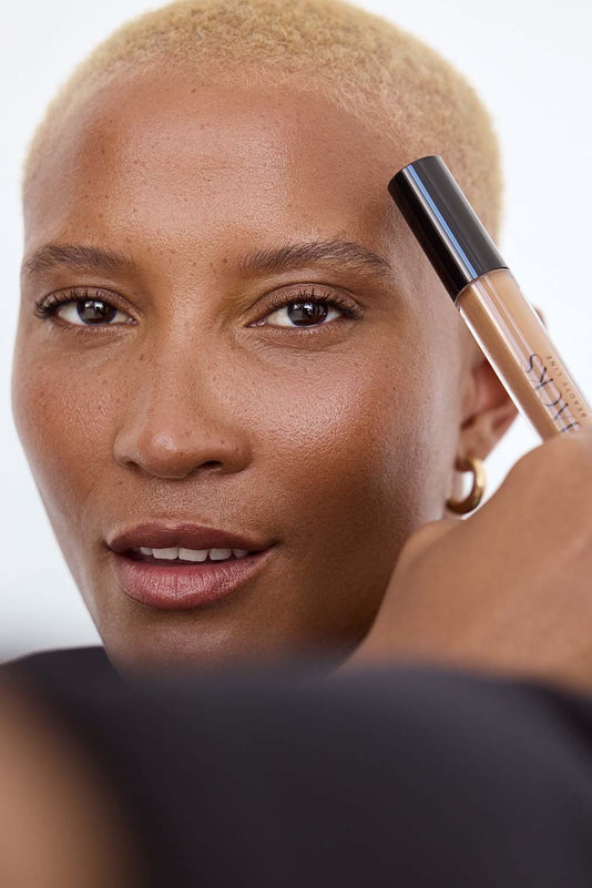 #farbwunsch_n-7, Schwarze Frau hält den JACKS beauty line Cream Concealer neben ihr Gesicht