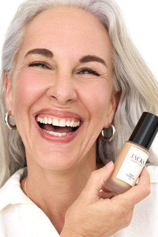#farbwunsch_n-3, #farbwunsch_mittlerer-bis-dunkler-hauttyp, Frau trägt JACKS beauty line Glow Foundation N4 im Gesicht und Flakon in der Hand