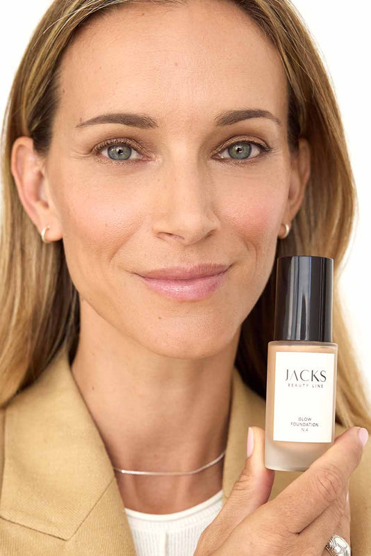 #farbwunsch_n-4, #farbwunsch_mittlerer-bis-dunkler-hauttyp, Frau trägt JACKS beauty line Glow Foundation N4 im Gesicht und Flakon in der Hand