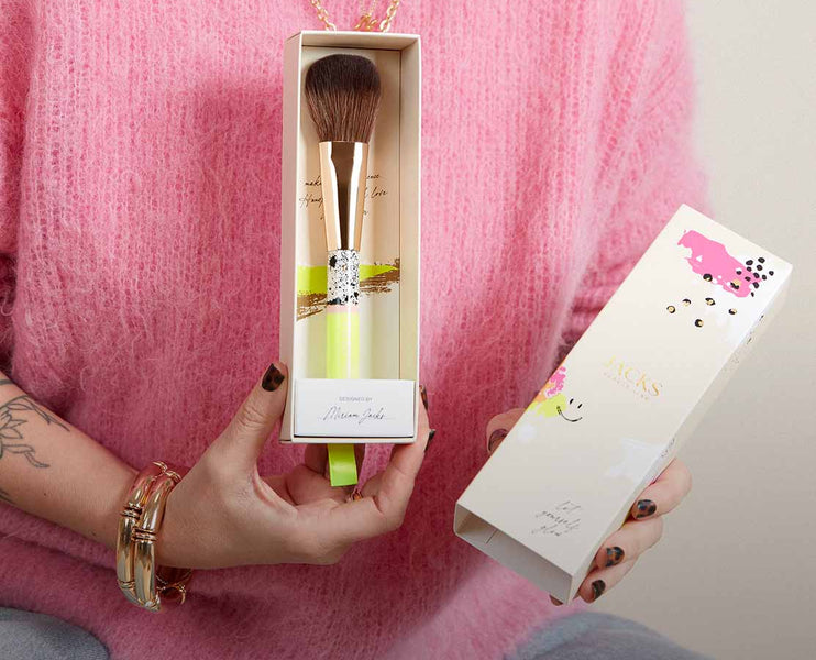 Frau hält einen handbemalten JACKS beauty line Puder- und Bronzerpinsel in einer besonderen Verpackung