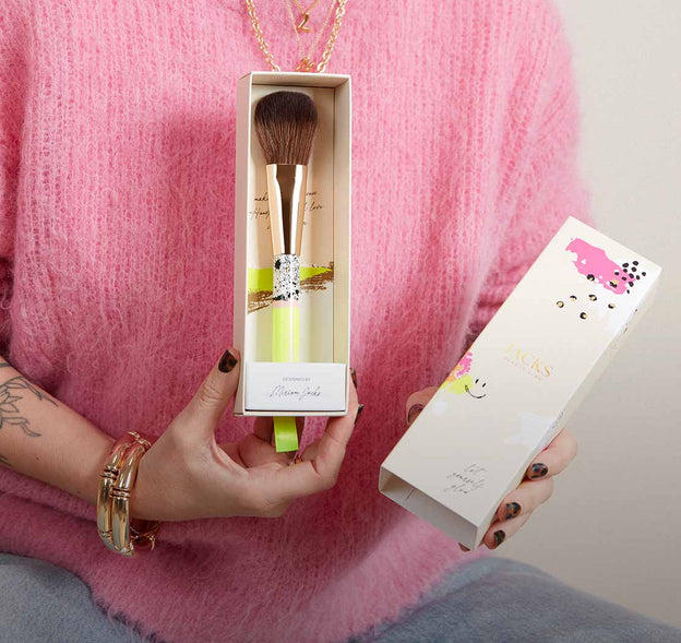 Frau hält einen handbemalten JACKS beauty line Puder- und Bronzerpinsel in einer besonderen Verpackung