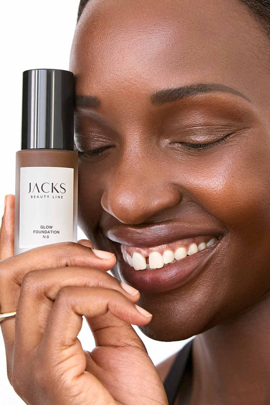 #farbwunsch_n-8, #farbwunsch_dunkler-hauttyp, Frau trägt JACKS beauty line Glow Foundation im Gesicht und Flakon in der Hand