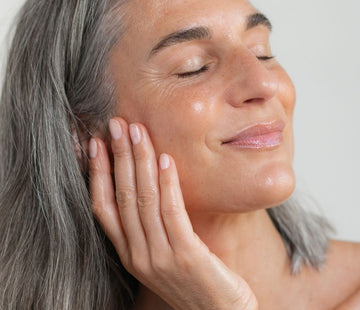 Eine Frau mit strahlender Haut lächelt mit geschlossenen Augen 