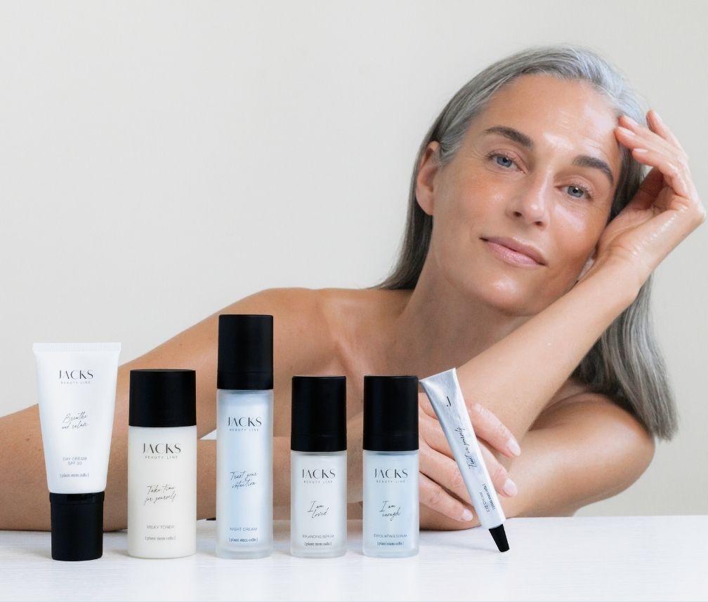 6 JACKS beauty line Skincare Produkte stehen vor einer älteren Frau mit strahlender Haut